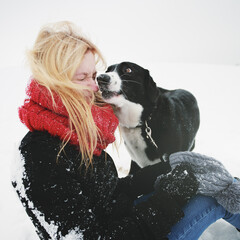 Young Caucasian woman playing with her dog in the snow in winter in the forest.