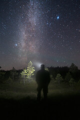 Fototapeta na wymiar Person silhouette with headlamp in forest looking out under clear night sky with Milky Way and stars