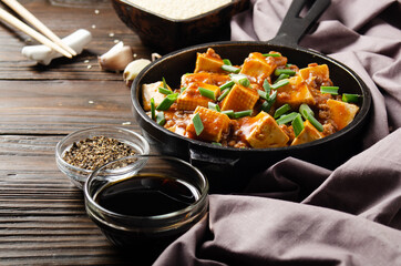 Mapo tofu in cast iron skillet with pork chopped chives soy sauce sichuan pepper garlic and spices closeup on wooden table
