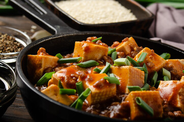 Mapo tofu dish with pork chives soy sauce garlic and spices closeup in cast iron skillet