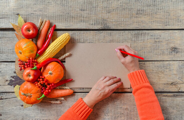 Autumn background, fallen leaves, fruits, vegetables on rustic wooden table. Woman hands with aged vintage paper and pencil, copy space. Thanksgiving food, healthy and fresh, top view, flat lay.