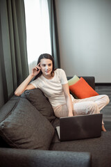 Fototapeta premium Young woman with modern laptop sitting on sofa at home