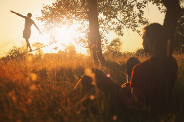 Two men practicing slackline in a field at sunset. Two friends doing sports at sunset.