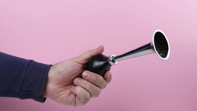 caucasian hand of a man with a vintage metal klaxon making  announcement against a pink background close-up. concept of alarm signal or warning
