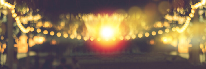 blurred bokeh light on sunset with yellow string lights decor in beach restaurant