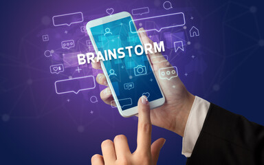 Female hand typing on smartphone with BRAINSTORM inscription, social media concept