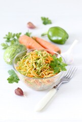 Korean vegetable salad with zucchini, pepper, carrot, garlic and parsley in a glass bowl on a white background