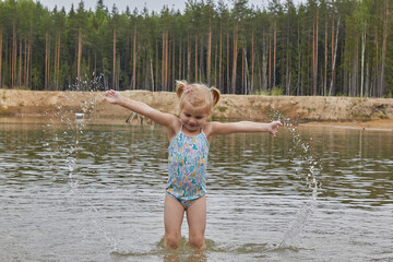 little girl in the water on the lake in the forest spray drops in nature