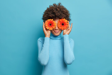 Photo of curly haired female florist has fun while makes decorations for special occasion, keeps...