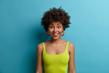 Horizontal shot of pretty optimistic woman has curly hair and looks surprisingly at camera with...