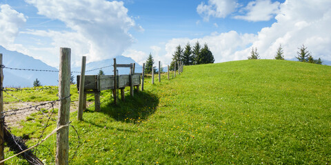 Fototapeta na wymiar Panorama einer Bergwiese durch die ein Holzzaun führt