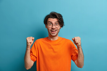 Hopeful man supports favorite football team, raises clenched fists and looks with excitement at...