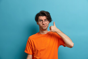Contact me by phone. Serious displeased man with trendy hairstyle makes call gesture near ear and...