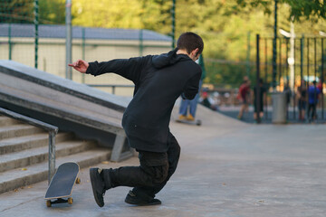 Skateboarder performed trick on city street. Young man jumped over obstacles - staircase, unsuccessful. He fell. Extreme sports- popular among youth. Back / rear view