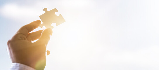 The man holds in his hand a jigsaw puzzle.