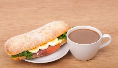 coffee cup and Real sandwich with smoked salmon, eggs and green on a wooden background.