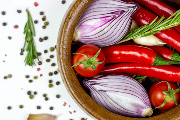 Top view of summer vegetables: onion, garlic, tomato, red chili pepper, rosemary in brown wooden bowl and peppercorns on white table background.