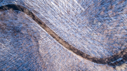 Aerial view of curved road in the snowy mountains. Top down view of frozen winter forest and a curvy road