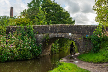 Cyclist walking under a stone foot bridge over a canal