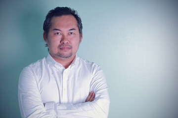 Asian businessman looks discreet standing cross arms on the green background. A man feeling confident of successful.