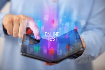 Young man holding a foldable smartphone with ONLINE TEST inscription, educational concept