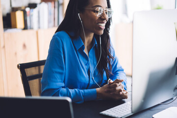 African American cheerful business female using computer with headphones