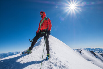 Last steps before Mont Blanc (Monte Bianco) summit 4,808m of smiling rope team man with climbing axe dressed mountaineering clothes,boots with crampons walking by snowy slopes with blue sky background