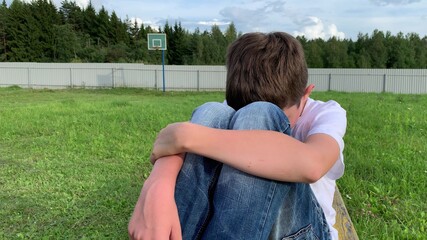 A lonely sad boy sitting outdoors on a bench, unhappy depressed child with discrimination and bullying problems