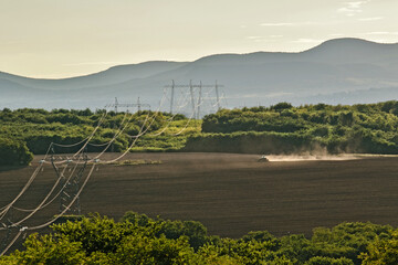 Autumn work in the fields with the tractor, dusting the air as it plows the ground. Long power lines through the field.