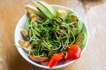 Vegan bowl with avocado, grilled tofu, zucchini and sweet potato, with greens and nuts on top