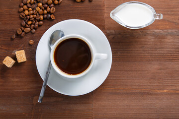 A cup of coffee on the table next to sugar and cream in a jug.