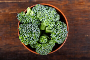 Fresh broccoli in a clay bowl on a wood background backdrop.