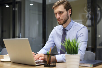 Young modern business man working using laptop while sitting in the office.