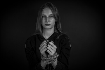 Portrait of young girl with bound hands on black background