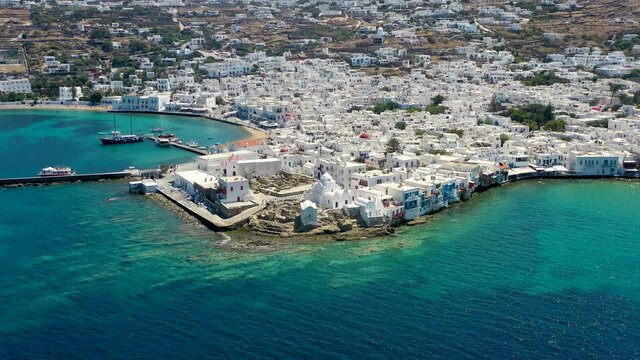 Aerial view of the old port and beautiful town of Mykonos island, Cyclades, Greece, with whitewashed houses next to the emerald colored sea