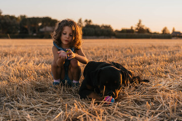 Young girl with brown hair sitting next to her dog during sunset.