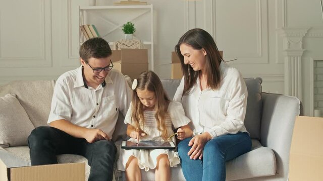 Teenage Girl Uses a Laptop During Sitting on a Sofa Between Her Parents. Modern Education. Data Protection.Financial Education of a Child.Cute Girl Studying Online on Laptop.Mutual Family's Purchases.