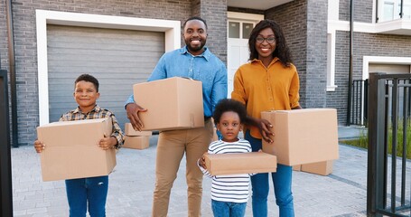 Portrait happy African American family with small children standing at new house at suburb and...