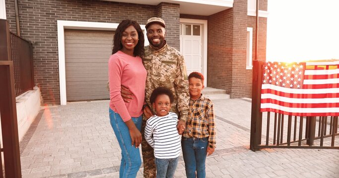 Portrait Of African American Family With Little Kids And Father Soldier. Outdoors In Yard At Home With USA Flag. Husband And Dad Coming Back Home From War. Male Officer With Wife And Small Children.