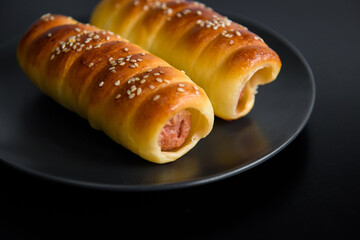 Sausage in the dough baked. Fast food photo subject on a black background.