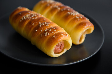 Sausage in the dough baked. Fast food photo subject on a black background.