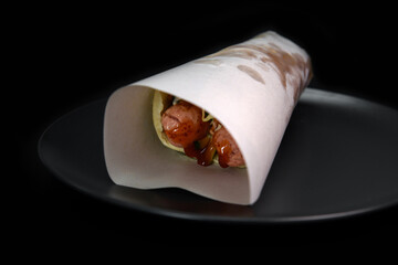 Flour tortilla with filling on a platter. Fast food photo subject on a black background.