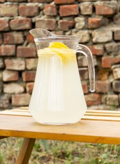 Lemonade in a glass jug / pitcher with lemon slices on a wooden table against the background of an...