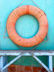 An old lifebuoy hanging on a green wall above an old blue wooden bench