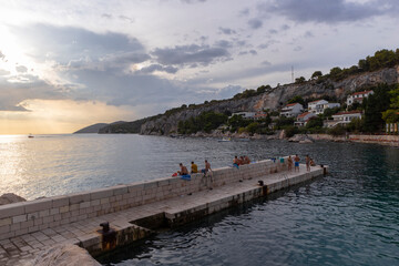 Hvar/ Croatia-August 9th, 2020: Beautiful sunset at Hvar island, observed by swimmers and people on the beach during summer tourist season - obrazy, fototapety, plakaty