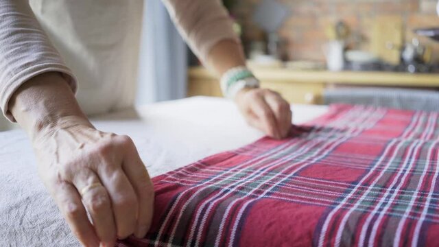 aged person hand with golden ring covers table with checkered tablecloth of purple colour against blurry lady putting black plate close view