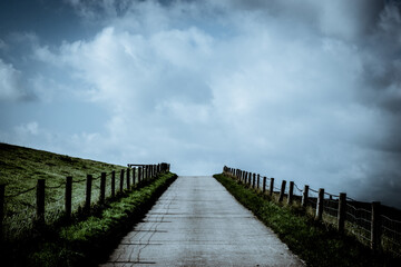 a lonely narrow road towards cloudy sky