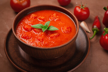 Bowl of traditional gazpacho soup with fresh tomatoes and peppers on brown background