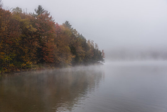 Lake with wooded shores shrouded in thick morning fog in autumn