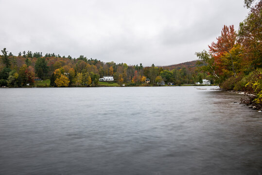 Mountain lake with forested shores dotted with holiday homes on a rainy autumn day. Autumn colours.